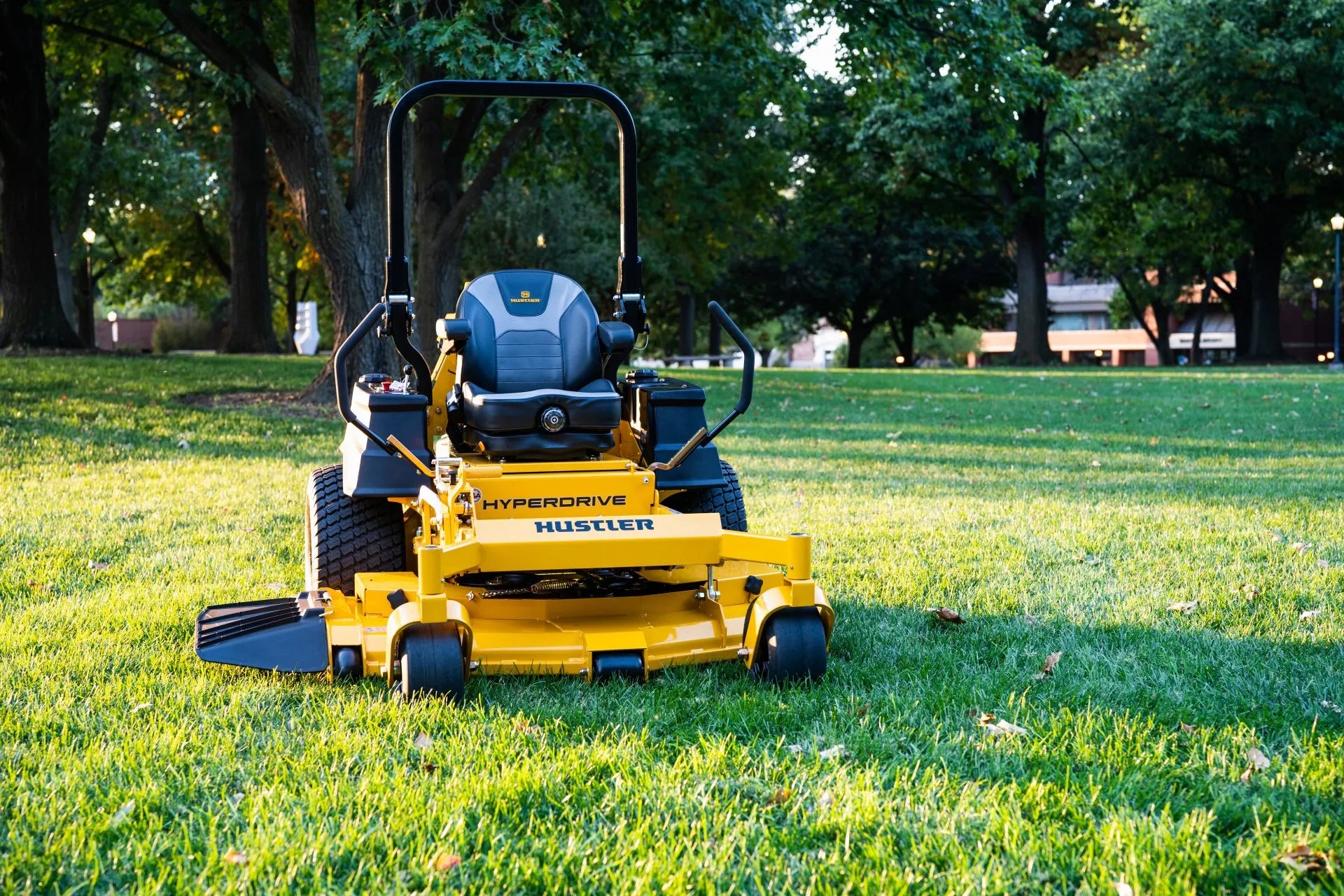 Yellow Hustler mower on a grassy field with trees in the background