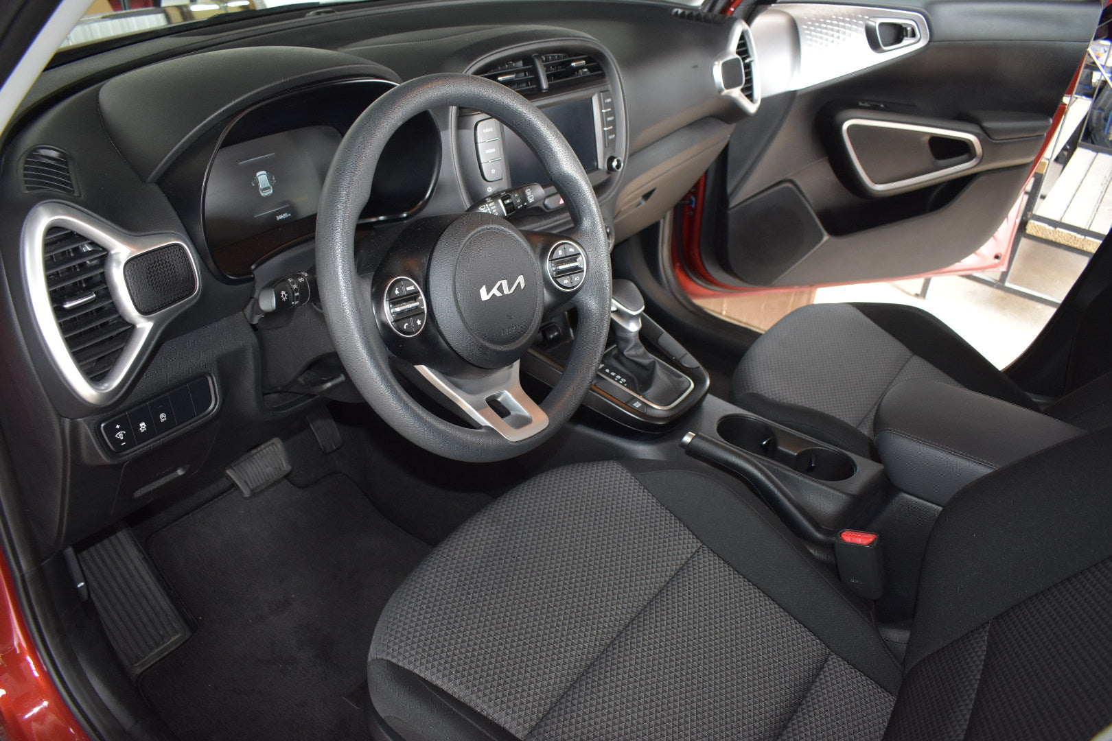 Car interior with steering wheel and dashboard, showing Kia logo.