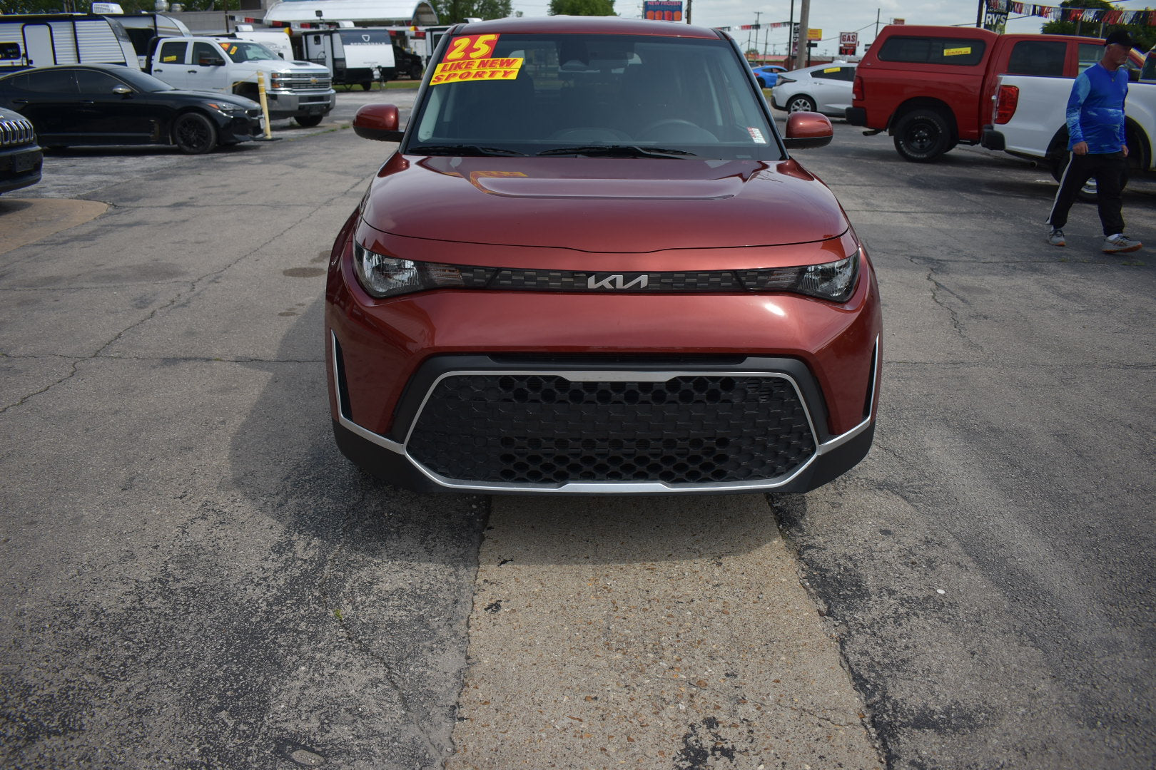 Red Kia vehicle parked in a lot with other cars and buildings in the background