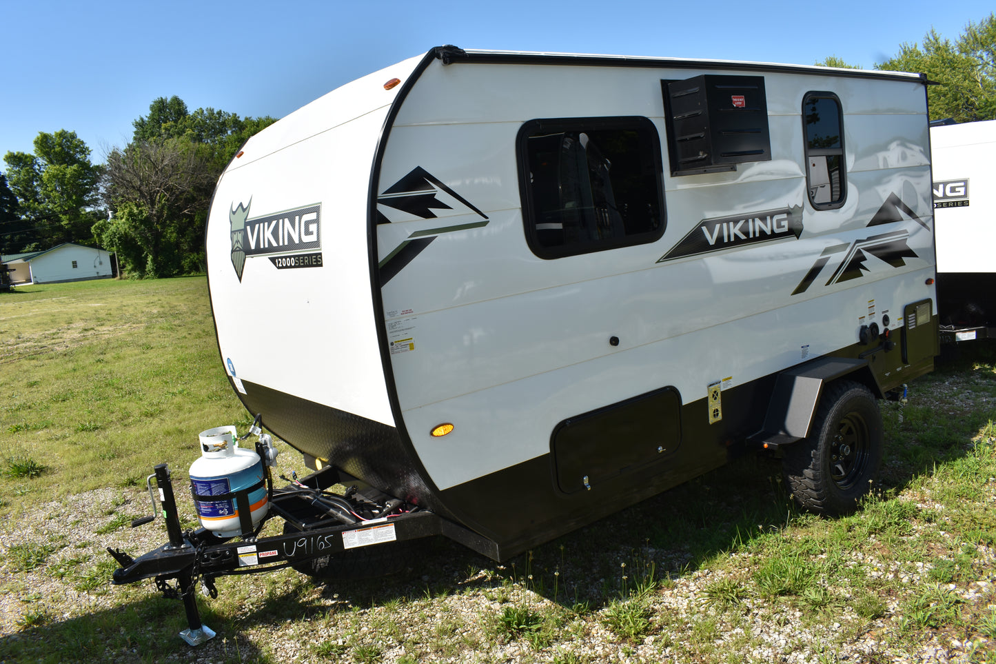 White and black Viking travel trailer parked on grass with trees in the background