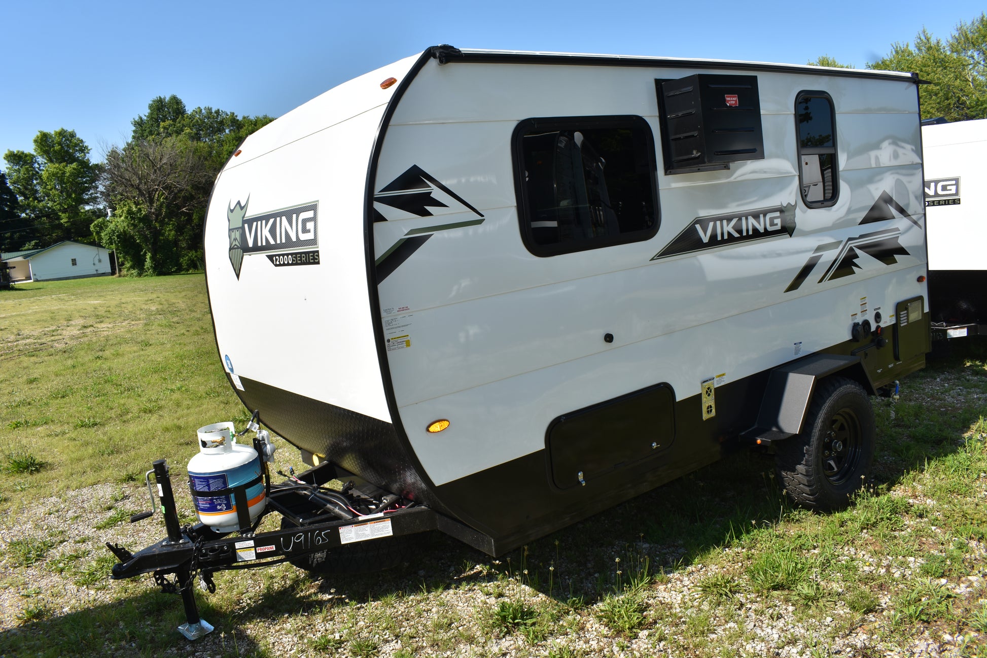 White and black Viking travel trailer parked on grass with trees in the background