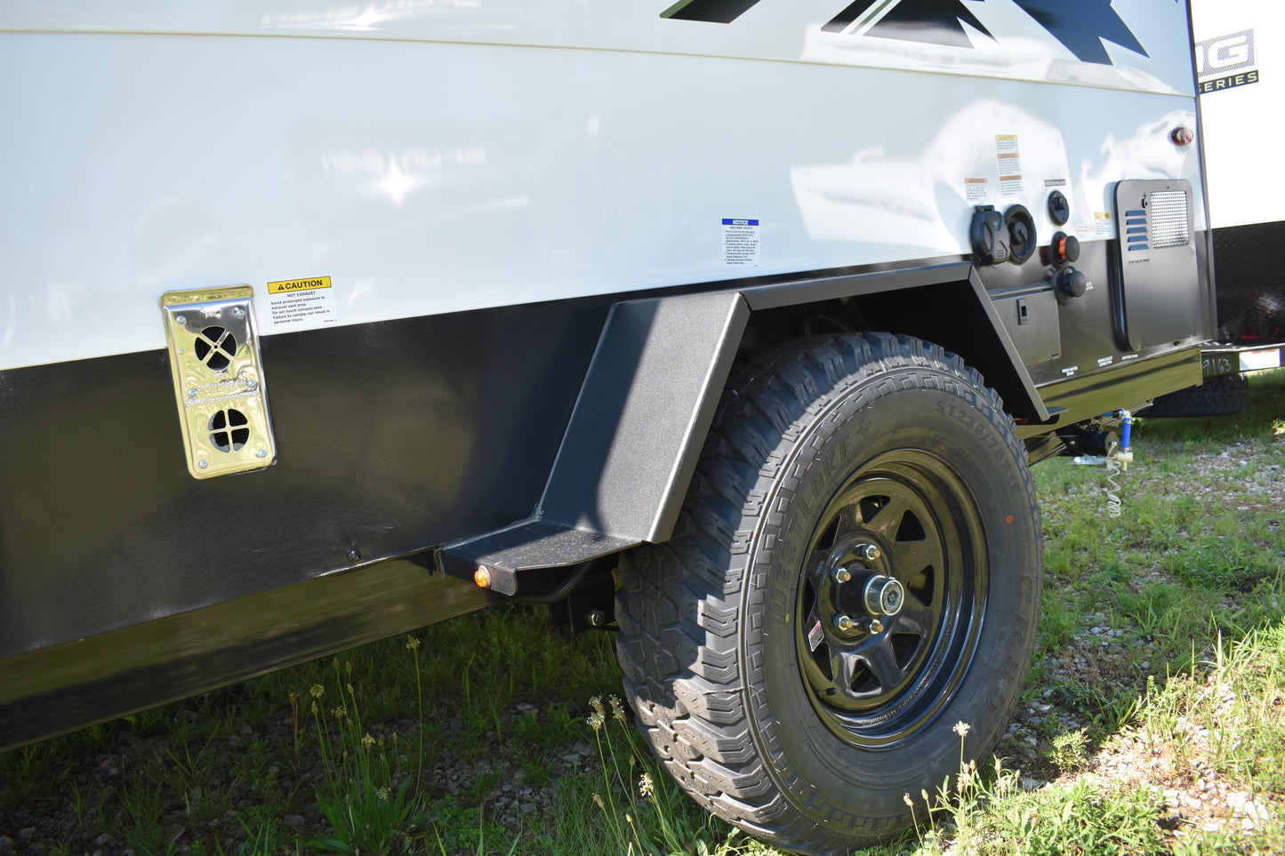 Back end of a white travel trailer with a tire and hitch on grass