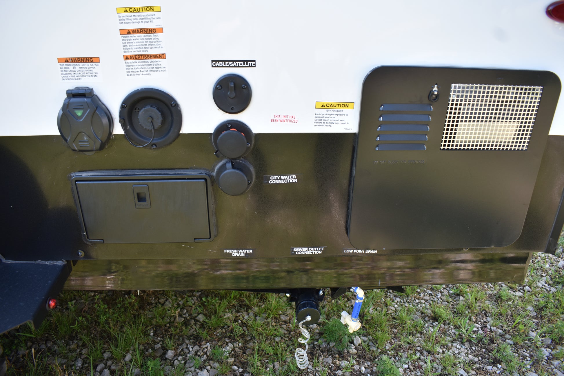 Back of a recreational vehicle with various components and labels on a grassy area.