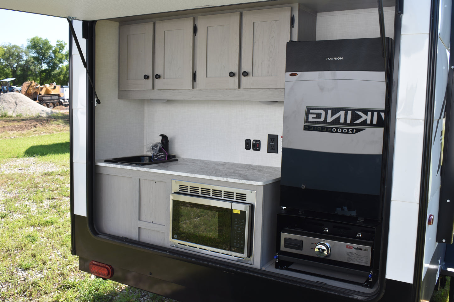 Compact kitchen area inside a recreational vehicle with cabinets, sink, and appliances.
