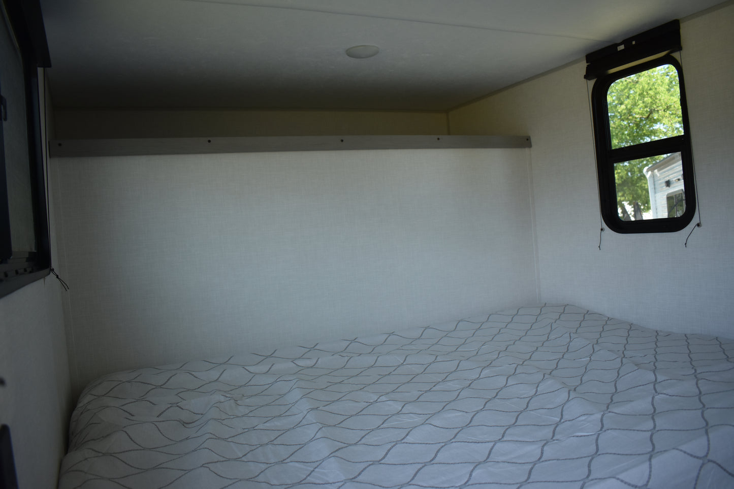 Small bedroom inside a vehicle with a mattress on the floor and a window showing greenery outside.