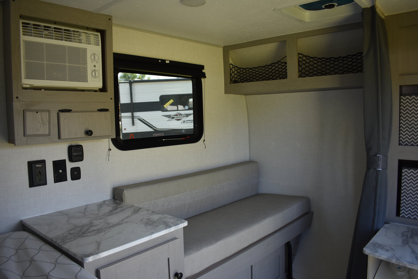 Interior of a compact living space with a bed, table, and small TV.