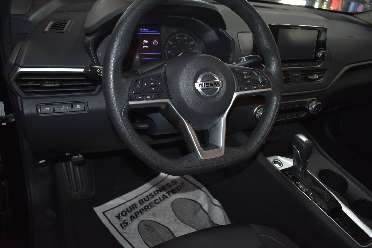 Car interior with steering wheel and dashboard, featuring a Nissan logo.