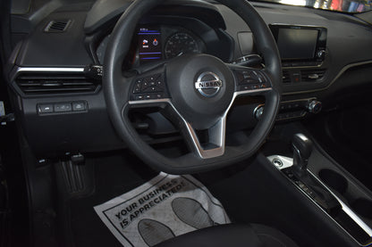 Car interior with steering wheel and dashboard, featuring a Nissan logo.