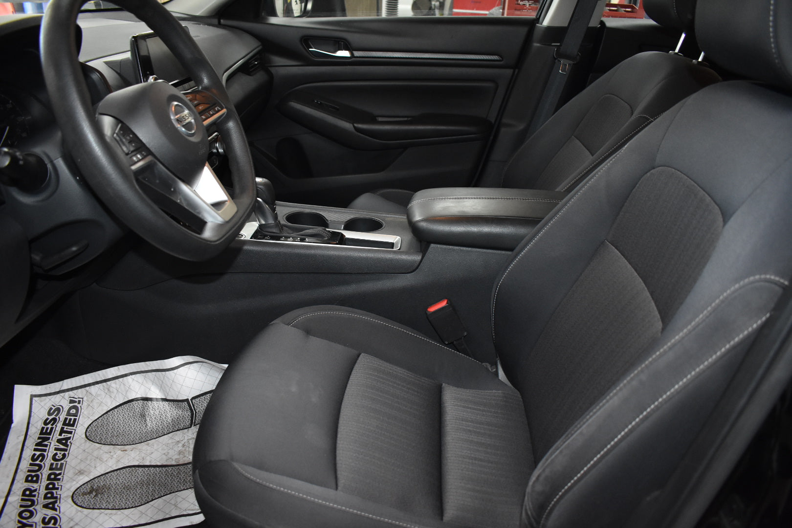 Car interior with steering wheel and dashboard, showing a branded towel on the floor.