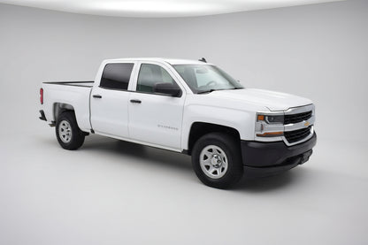 White Chevrolet Silverado truck parked in a parking lot with a gas station in the background.