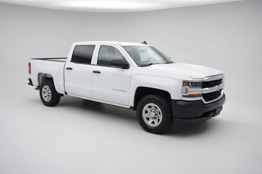 White Chevrolet Silverado truck parked in a parking lot with a gas station in the background.