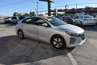 White car parked in a gas station lot with other vehicles and a clear sky.