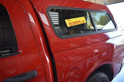 Red vehicle with a window sticker displaying 'abcmotors.com' in a showroom setting