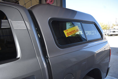 Close-up of a gray truck bed with a window, showing a yellow sign with text.