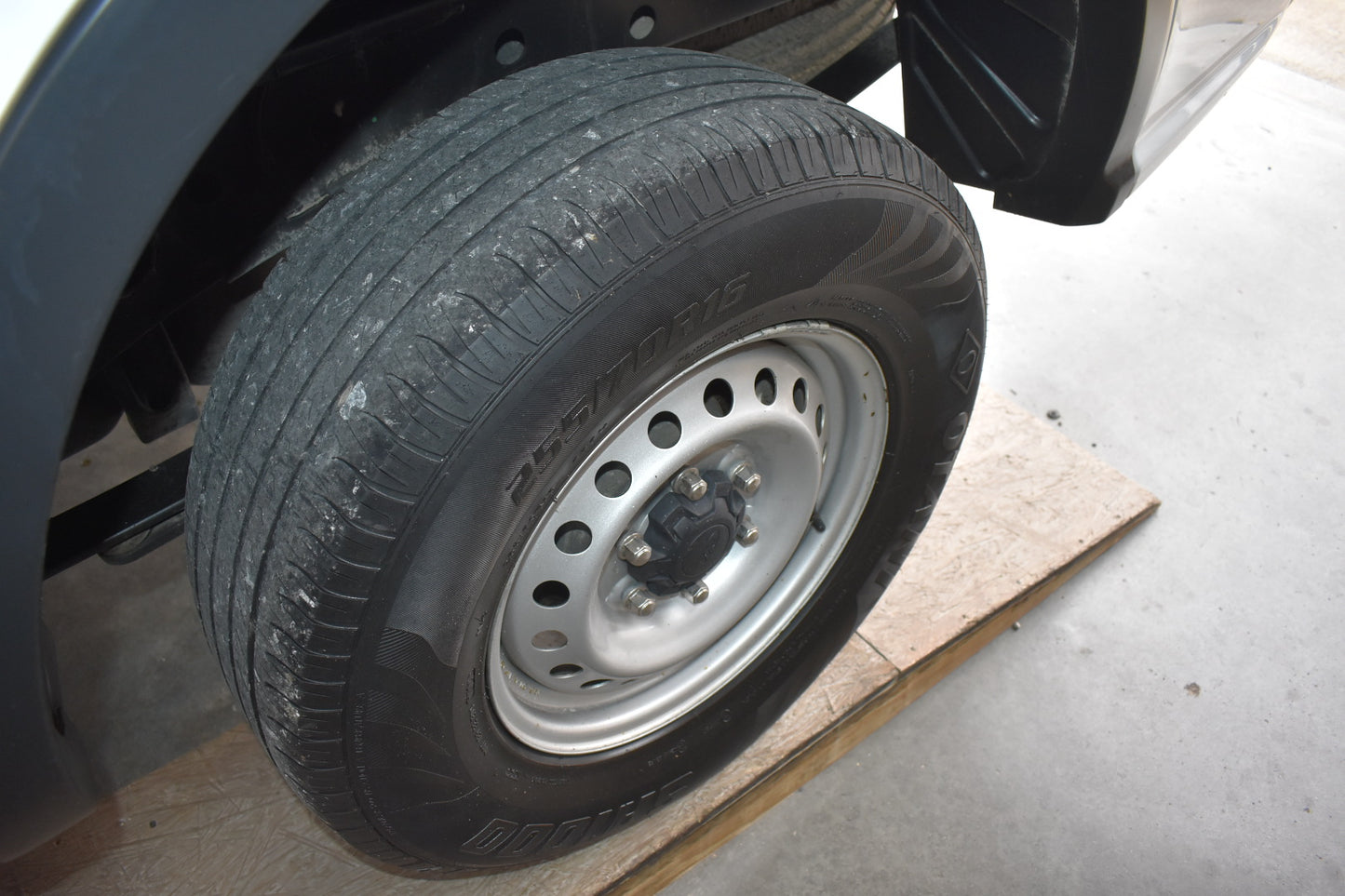 Car tire on a cardboard piece with a vehicle part in the background