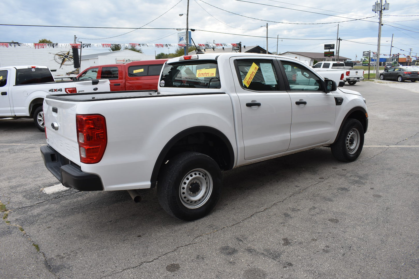 White pickup truck in a lot with other vehicles and a cloudy sky.