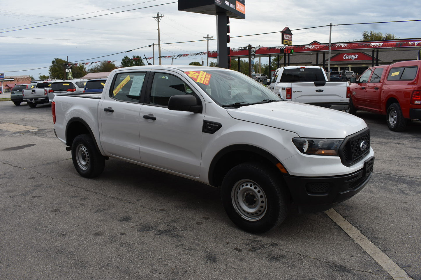 White pickup truck parked in a lot with other vehicles and a gas station in the background.