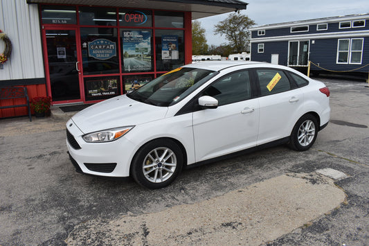 White car parked in front of a building with a 'For Sale' sign.