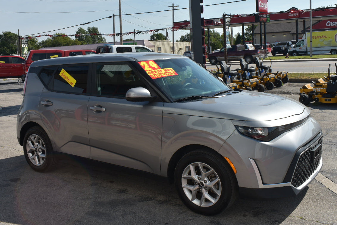 A silver compact SUV parked on a dealership lot with a yellow price sticker on the windshield, with construction equipment and a building in the background.