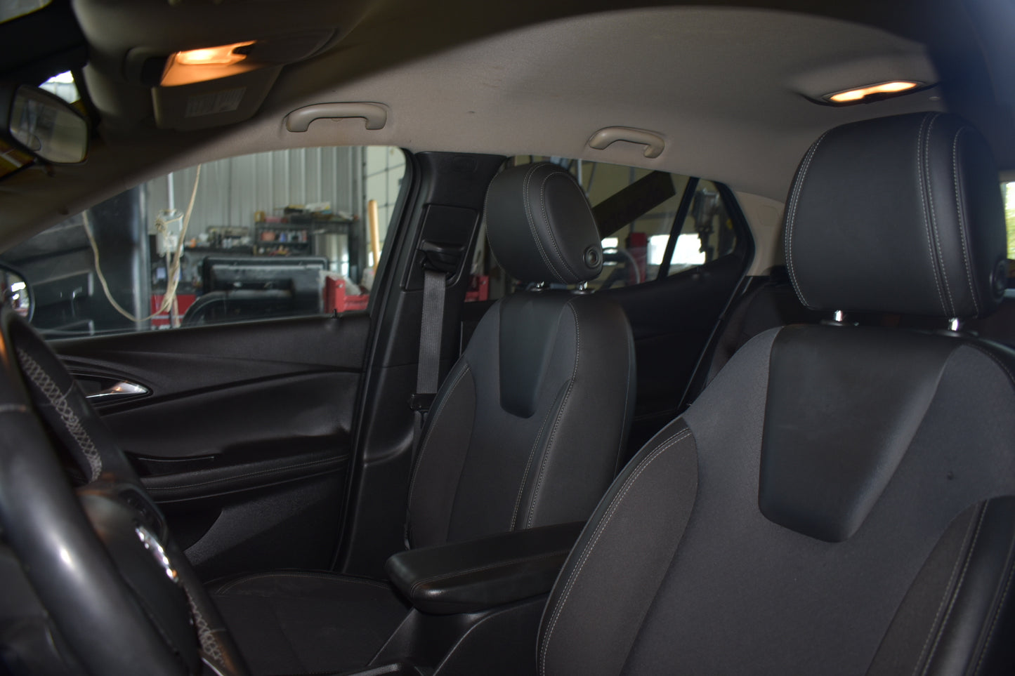 Black leather car seats inside a vehicle, showing the front passenger and driver seats with headrests, center console armrest, and interior door panel.