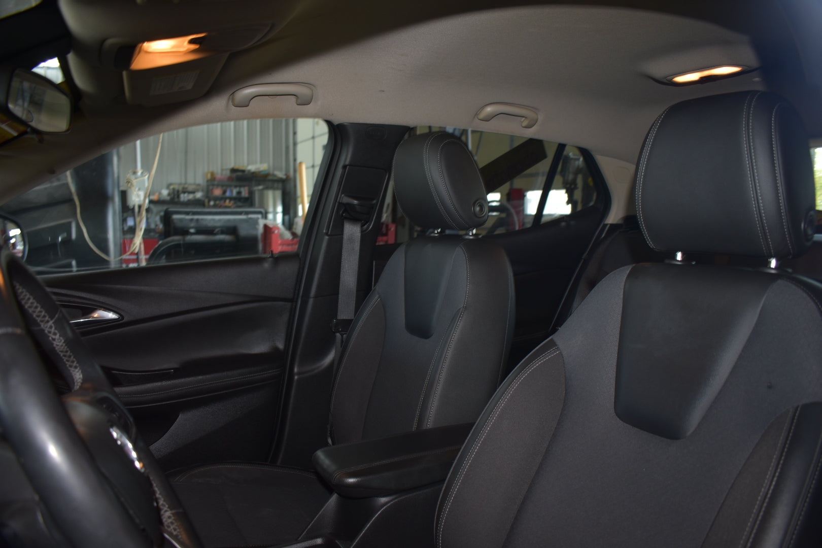 Black leather car seats inside a vehicle, showing the front passenger and driver seats with headrests, center console armrest, and interior door panel.