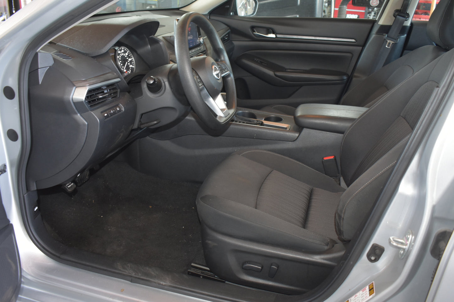 The interior of a vehicle shown from the open driver's side door, featuring black fabric front seats, a dark gray dashboard, and a center console.