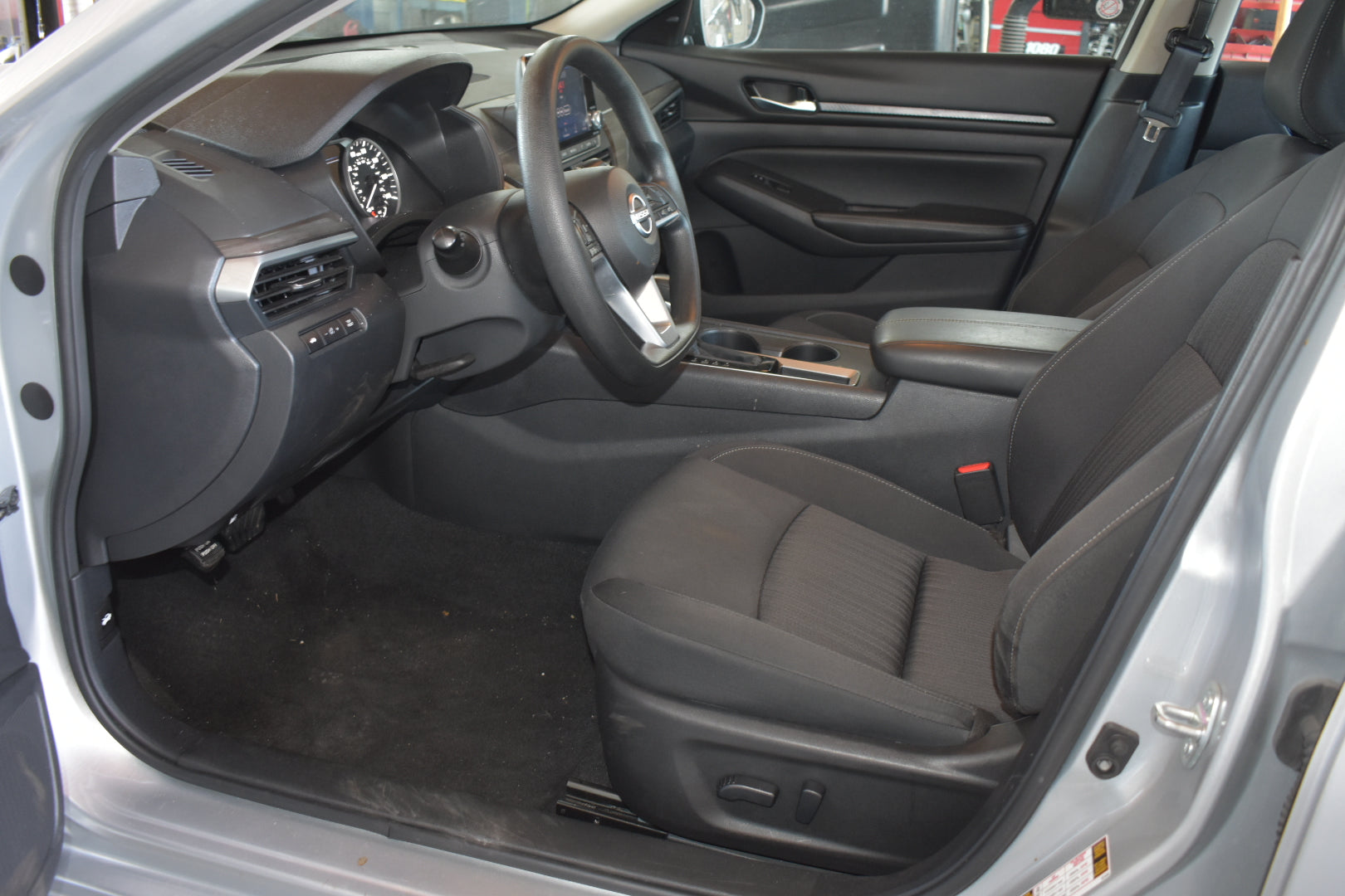 The interior of a vehicle shown from the open driver's side door, featuring black fabric front seats, a dark gray dashboard, and a center console.