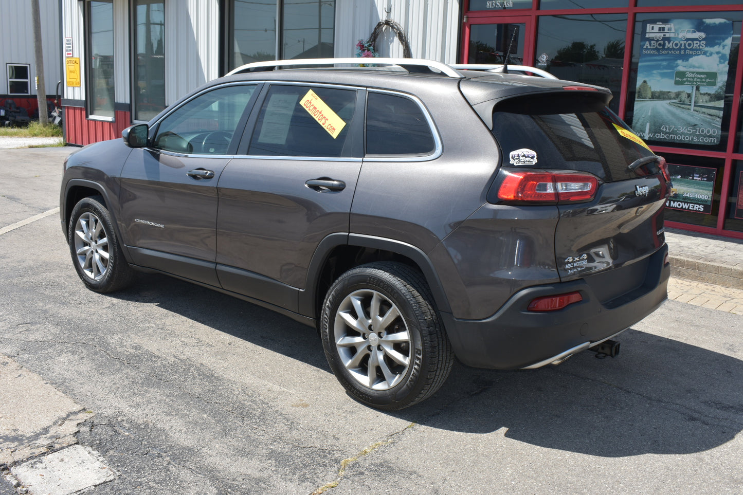 A dark gray 2018 Jeep Cherokee SUV parked on asphalt in front of a dealership building, viewed from a rear three-quarter angle.