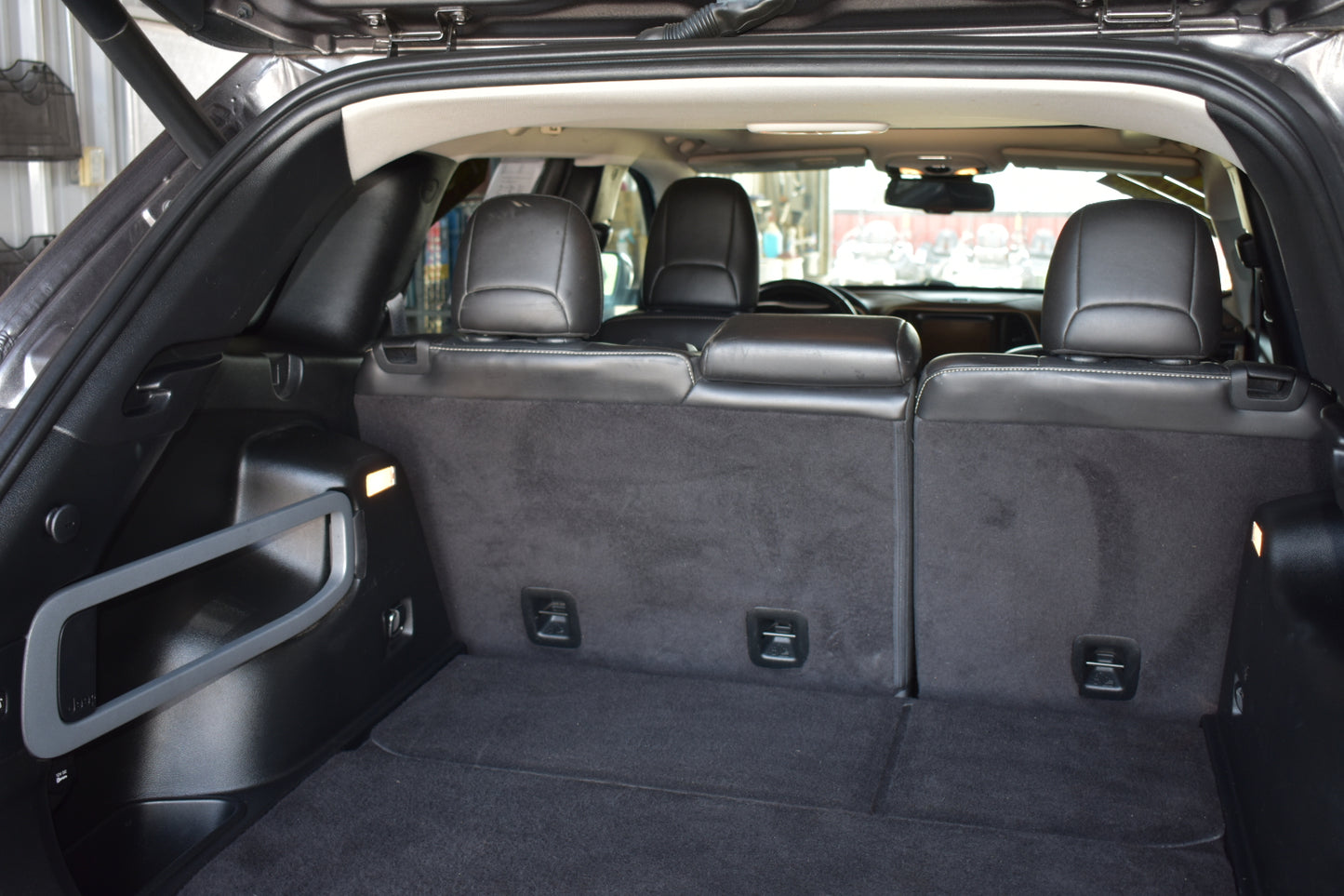 The rear cargo area of a black SUV with the third-row seats folded down, showing a spacious flat floor and dark gray carpeted trunk space.