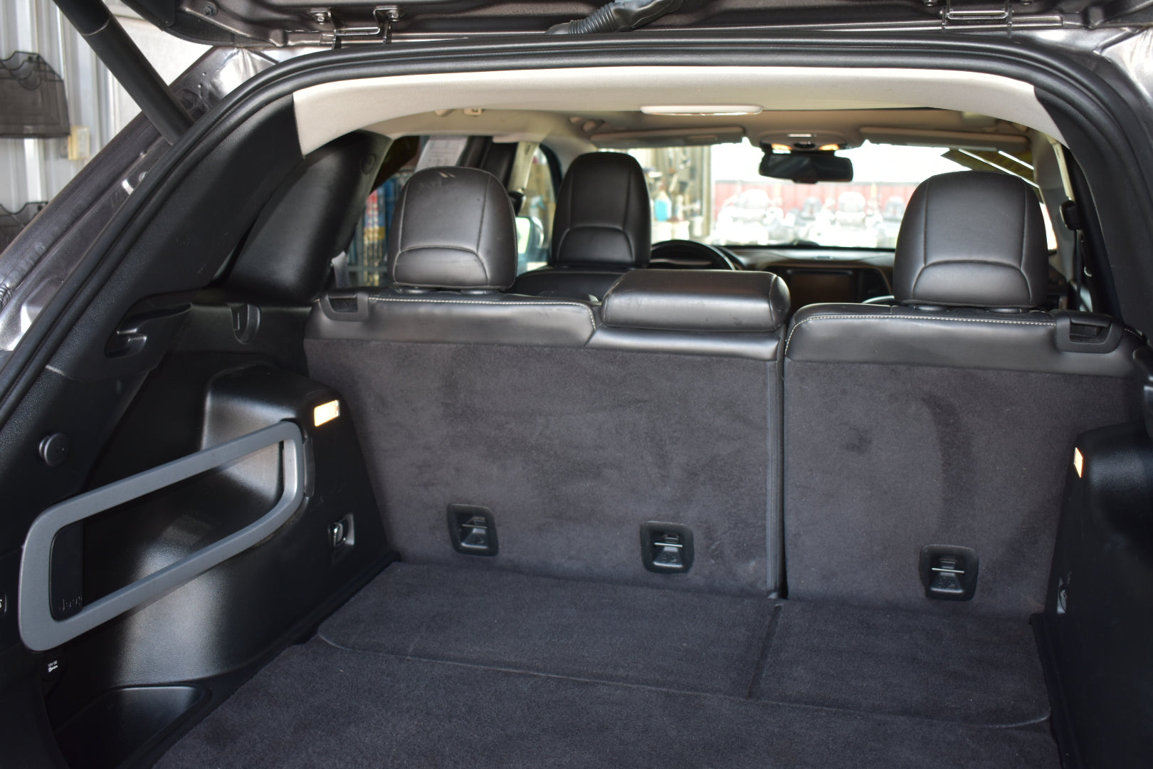 The rear cargo area of a black SUV with the third-row seats folded down, showing a spacious flat floor and dark gray carpeted trunk space.