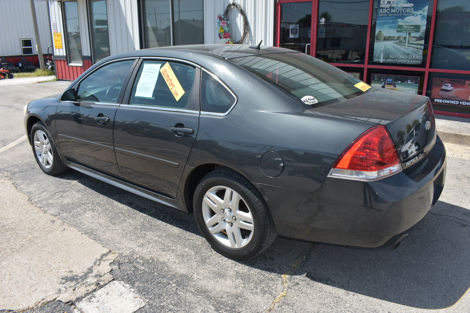 A dark gray Chevrolet Impala sedan parked outdoors on a paved lot in front of a dealership building, viewed from a rear three-quarter angle.