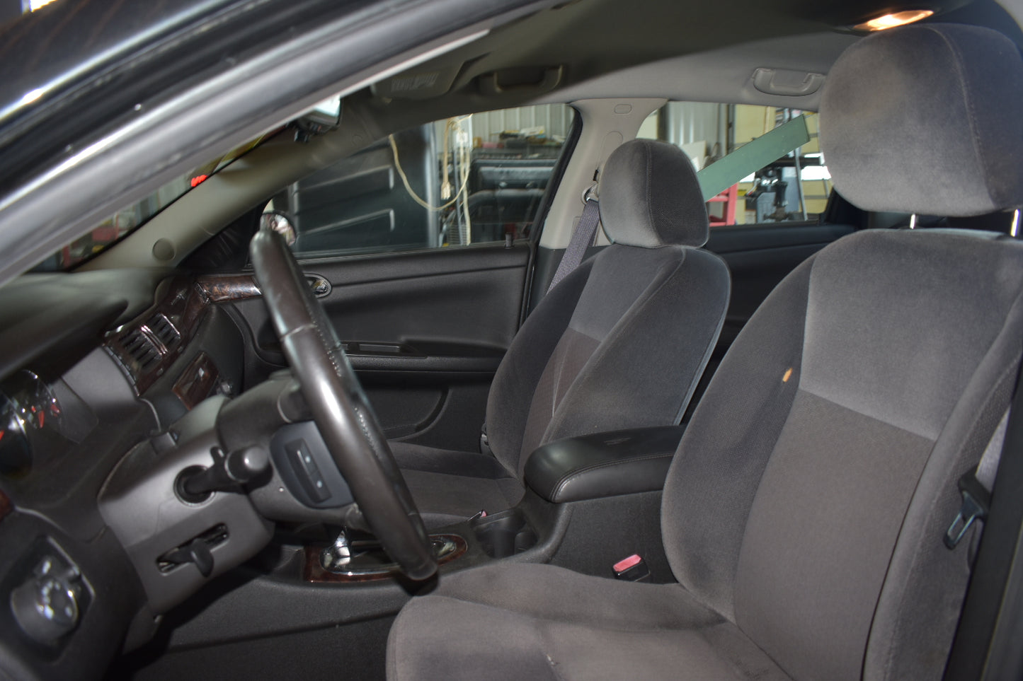 A dark gray fabric car interior with two front seats, a black steering wheel, and a gray dashboard, photographed from the open driver's side door.