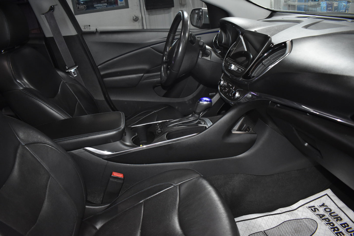 Car interior with steering wheel, dashboard, and floor mat.