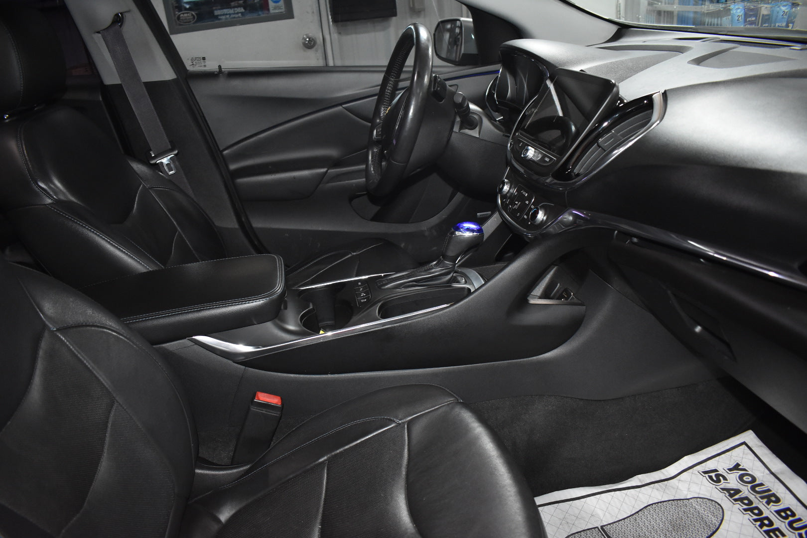 Car interior with steering wheel, dashboard, and floor mat.