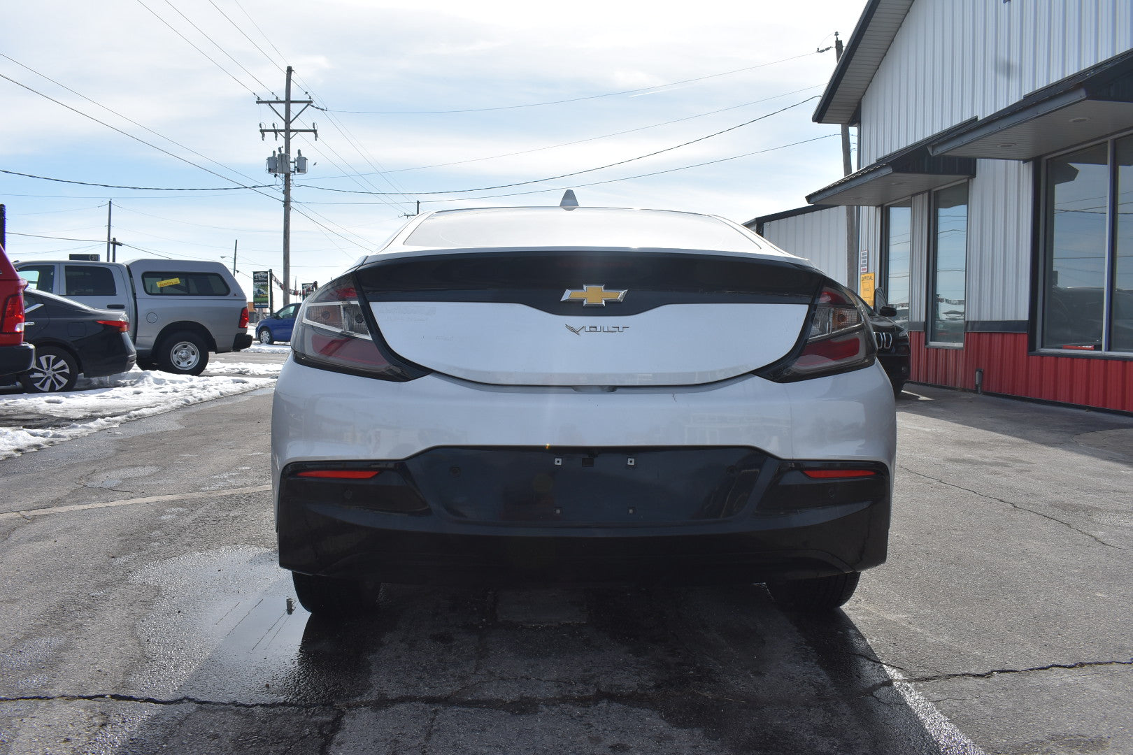 Back view of a white Chevrolet vehicle parked on a street with buildings and other cars in the background.