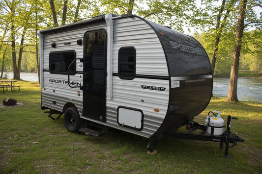Small travel trailer with 'Sportmen' branding on a dirt lot.