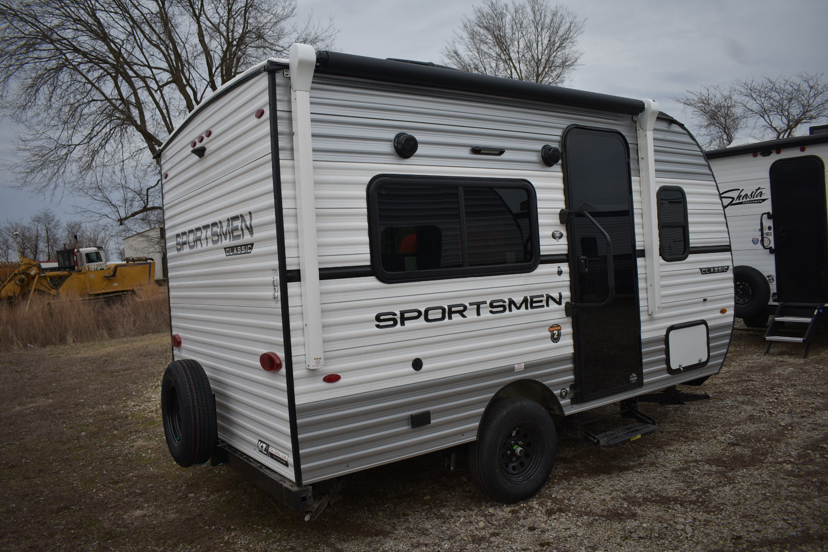 Small travel trailer with 'Sportsmen' branding on a dirt lot.