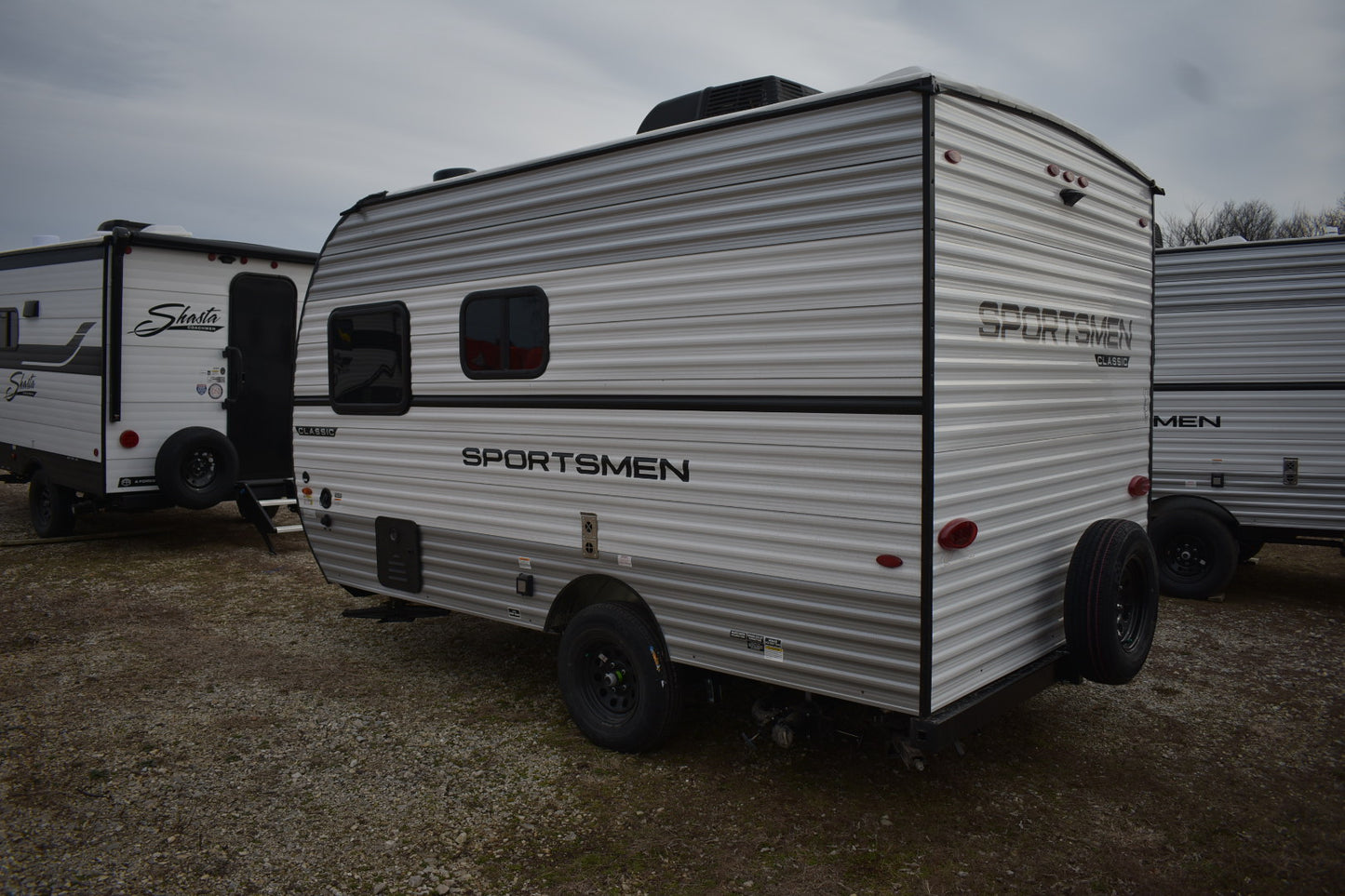 Small travel trailer with 'Sportsmen' branding on a gravel surface.