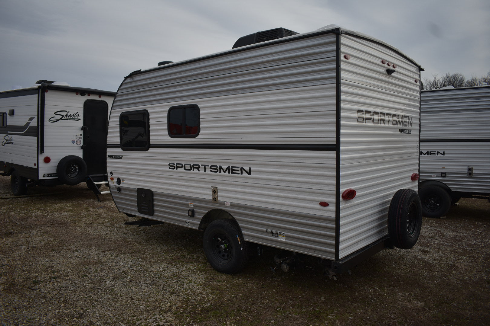 Small travel trailer with 'Sportsmen' branding on a gravel surface.