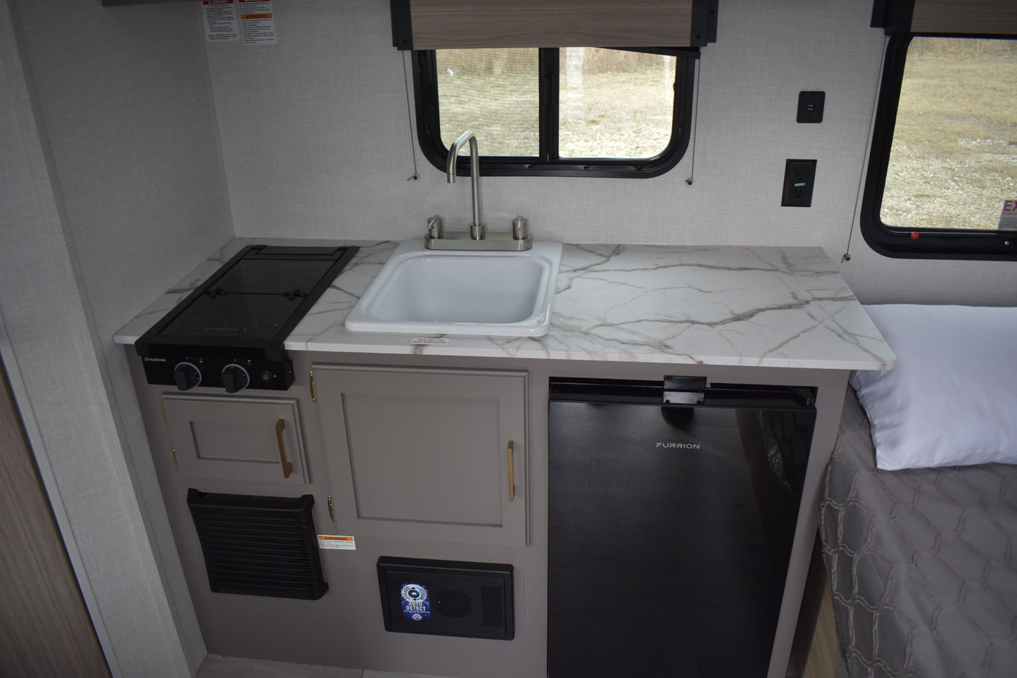 Compact kitchen area inside a vehicle with sink, stove, and refrigerator.