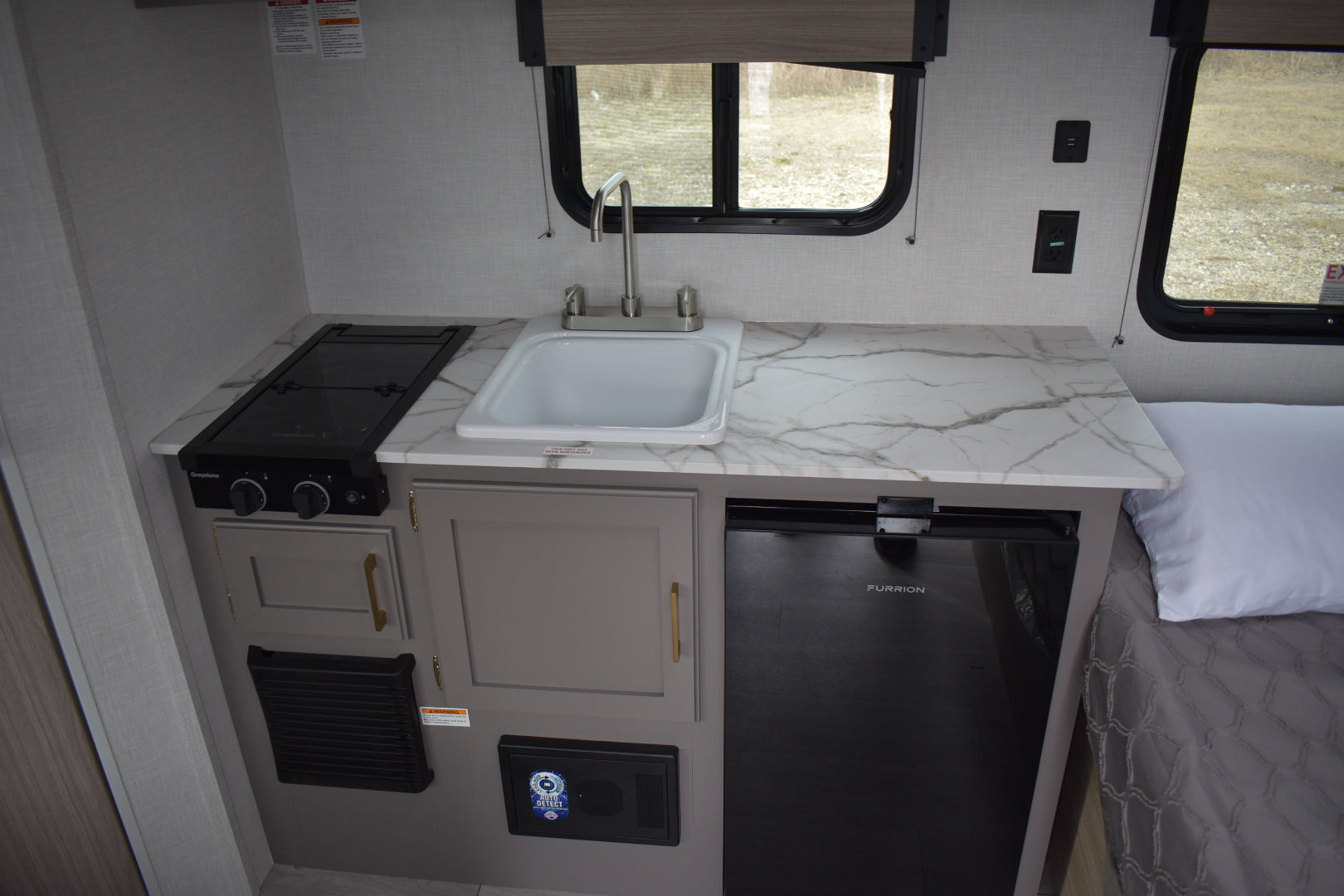Compact kitchen area inside a vehicle with sink, stove, and refrigerator.