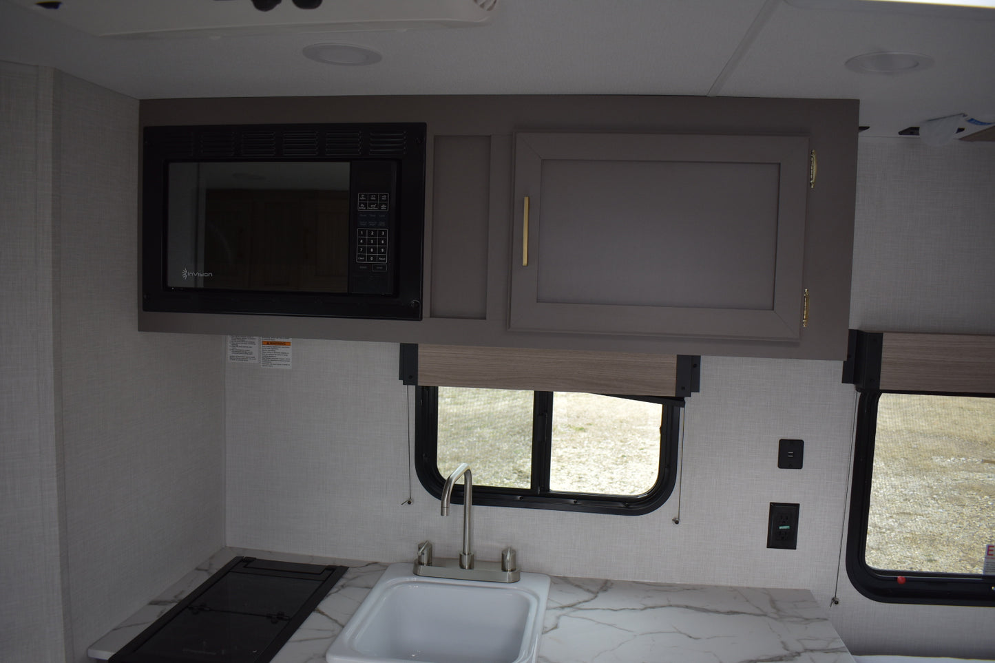 Compact kitchen area inside a vehicle with microwave, sink, and cabinets.