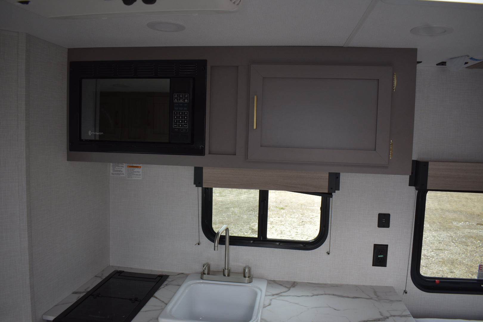 Compact kitchen area inside a vehicle with microwave, sink, and cabinets.