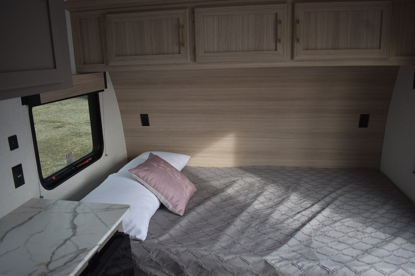 Bedroom interior of a vehicle with wooden cabinets and a small window.
