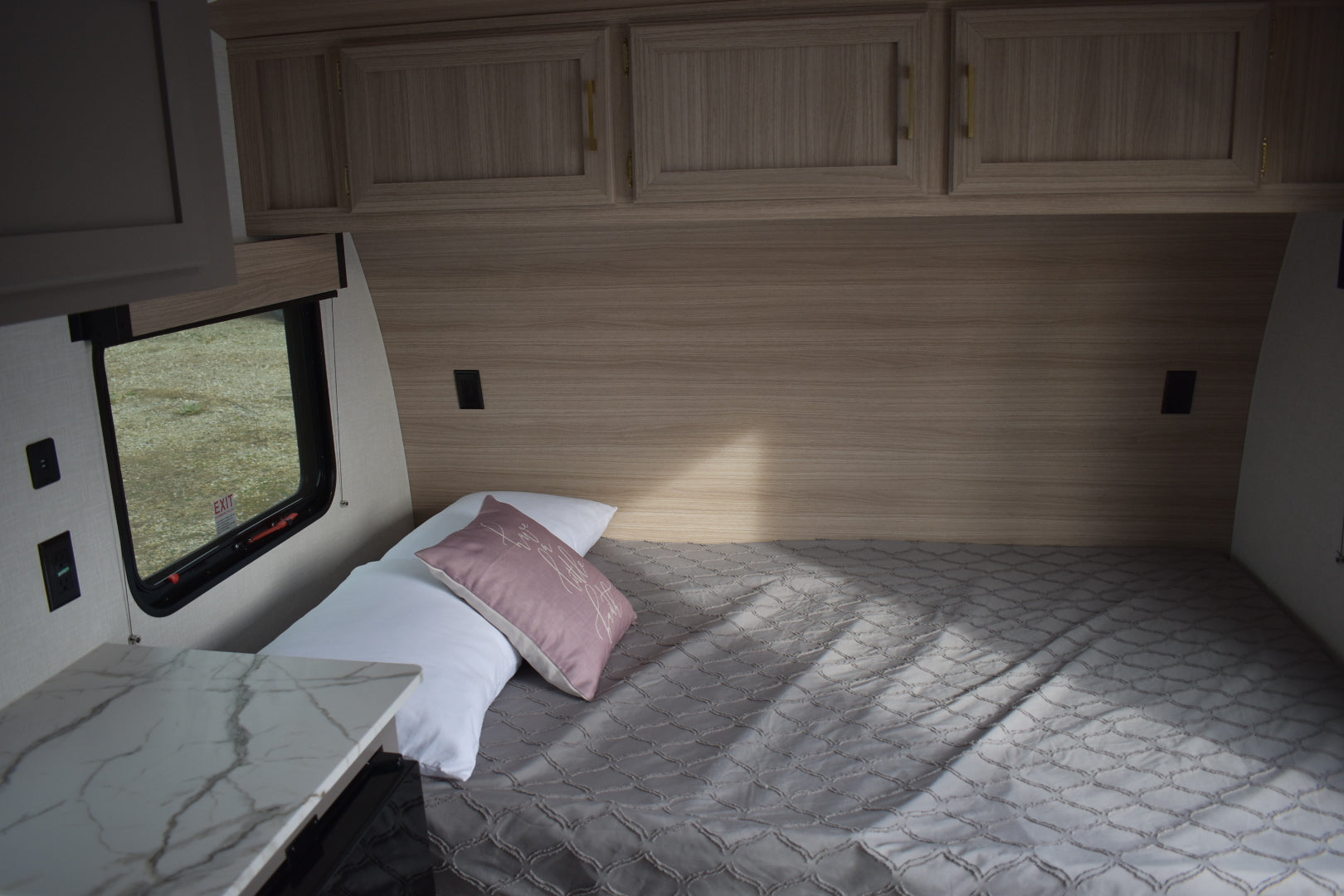 Bedroom interior of a vehicle with wooden cabinets and a small window.