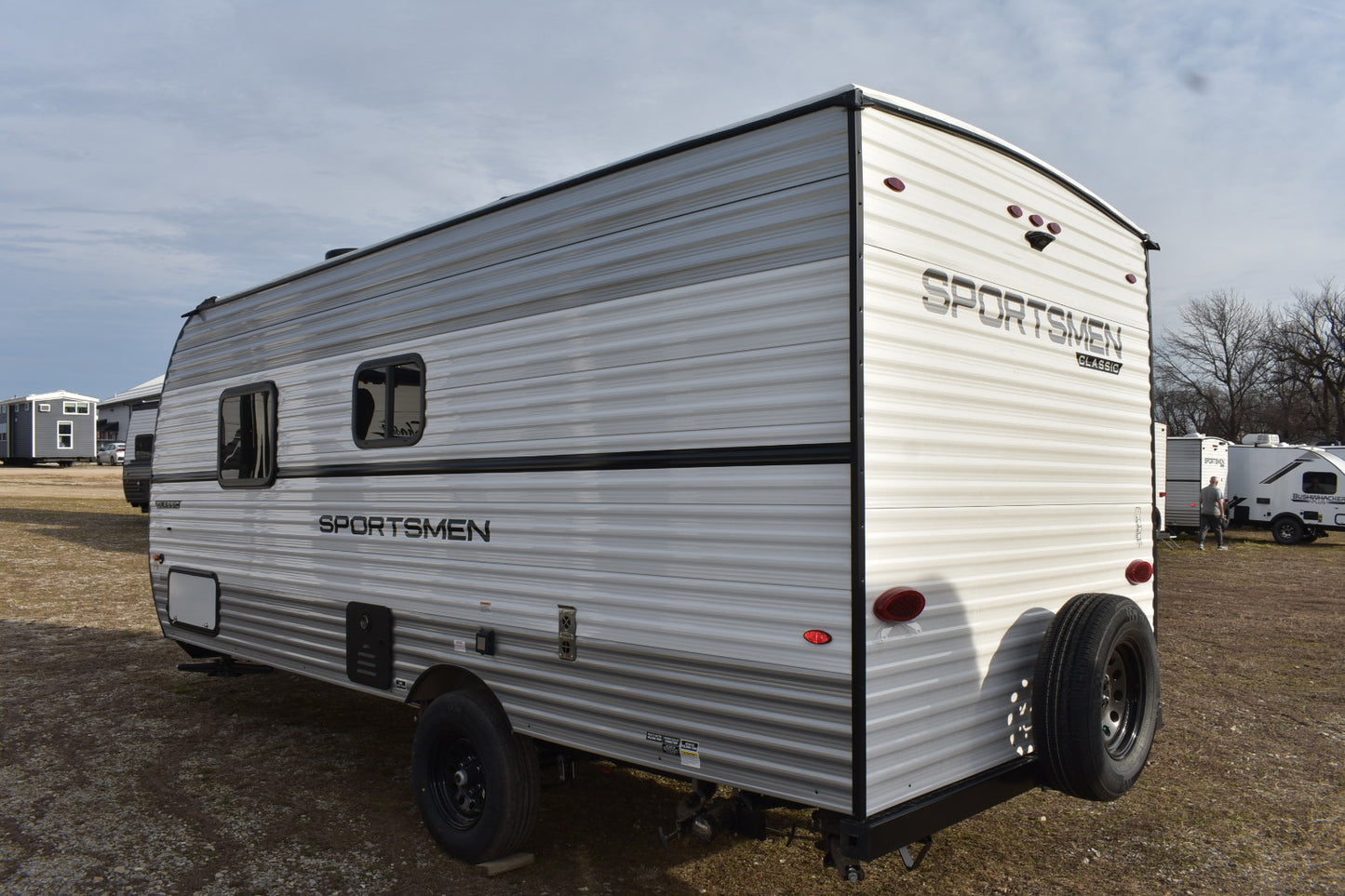 White travel trailer with 'Sportsmen' branding on a dirt field.