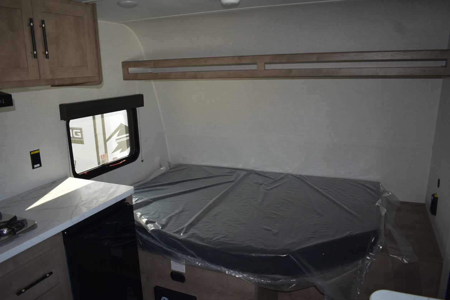 Compact living space with a bed covered in plastic wrap, kitchen area, and window.