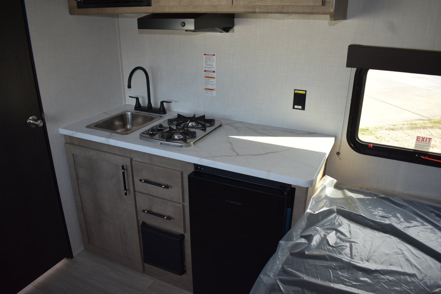 Compact kitchen area inside a vehicle with sink, stove, and cabinets.