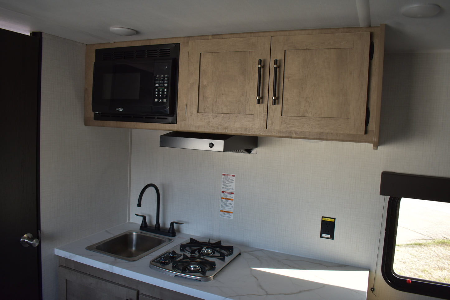 Compact kitchen inside a vehicle with cabinets, microwave, stove, and sink.