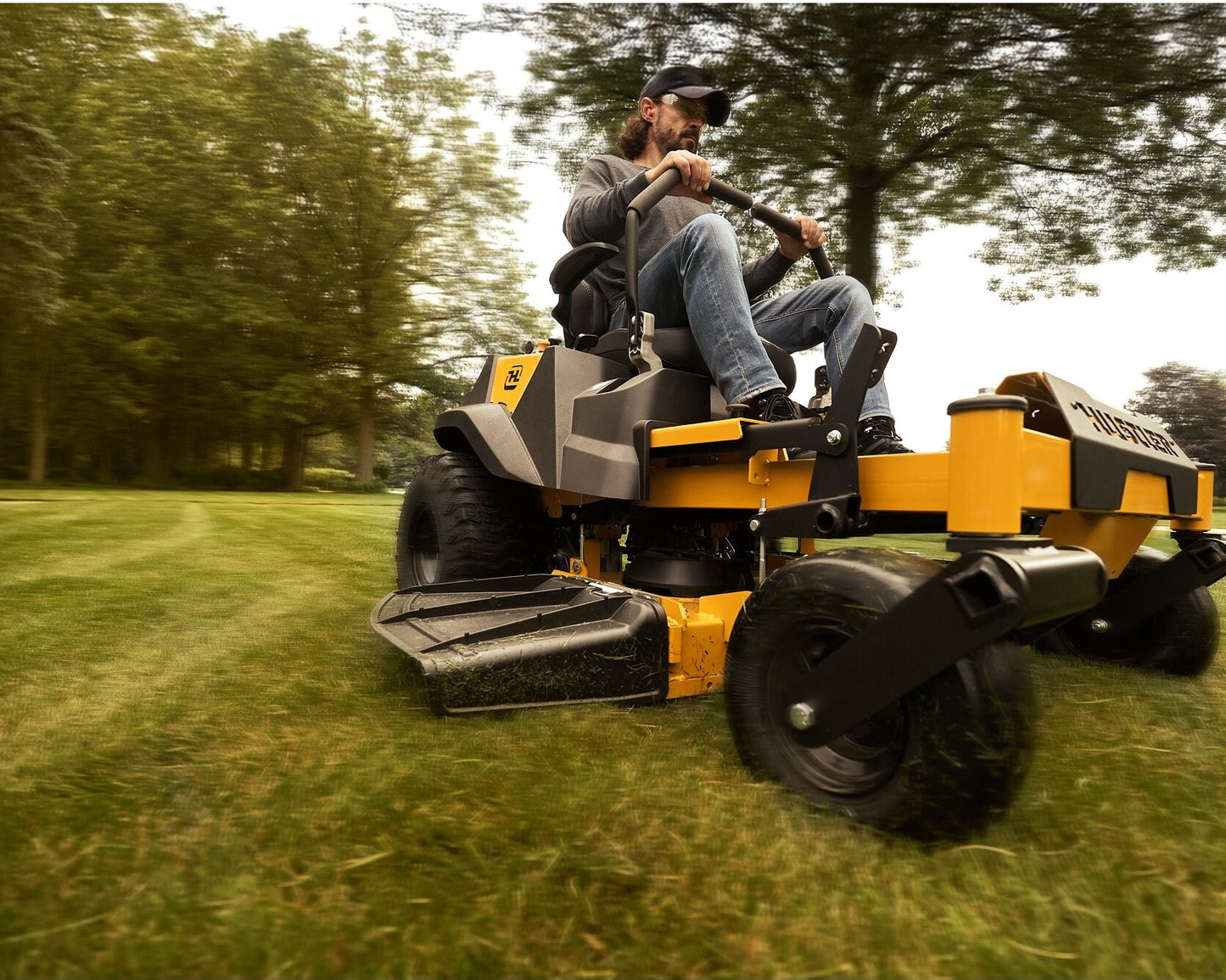 Person operating a yellow riding lawn mower on a grassy field with trees in the background